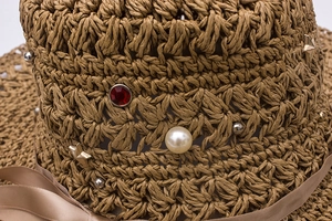 Détail de chapeau de paille avec strass rouges, perles et rivets en forme d'étoile