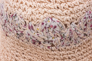 Macro detail of hand-woven beige straw hat featuring delicate floral fabric ribbon trim