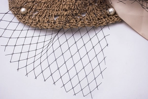 Détail du voile en maille noire avec perles et ruban en soie sur un chapeau de paille