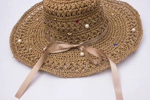 Détail d'un chapeau de paille au crochet avec perles, strass colorés et ruban champagne