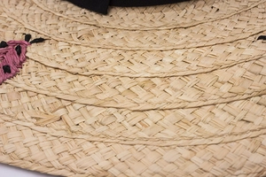 Close-up of woven straw sun hat with black ribbon and floral embroidery detail