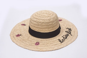 Close-up of woven straw hat with ladybug embroidery and elegant black ribbon detail