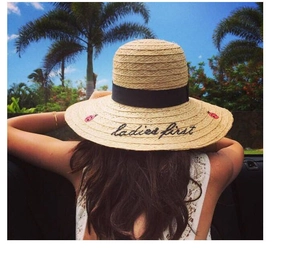 Detail of wide brim straw hat featuring black ribbon and 'ladies first' embroidery