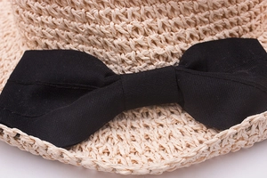 Detailed close-up of beige raffia sun hat texture and elegant black fabric bow tie