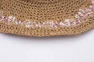 Close-up of straw sun hat featuring woven floral fabric trim and rustic paper texture