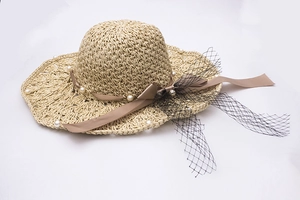 Détail d'un chapeau de paille beige avec perles, nœud en soie et voile en résille noire