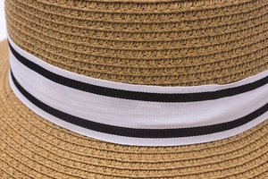 Detail of woven straw sun hat featuring a beige texture and white striped ribbon band