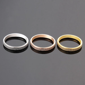 Three minimalist matte titanium steel rings in silver, rose gold, and gold on dark surface