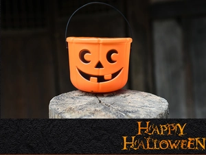 Detail of an orange plastic Halloween pumpkin bucket with a black handle on a wood stump