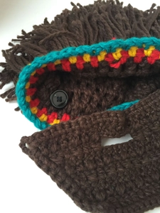 Close-up of knit beard hat with colorful fringe, braided patterns and a black button detail