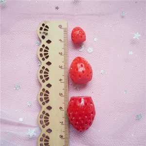 Detailed size comparison of three resin strawberry charms against a wooden ruler measure