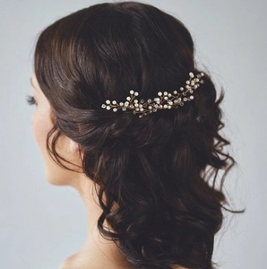Close-up of a gold bridal hair comb with white pearls and crystals on dark wavy hair