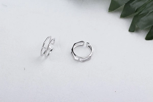 Close-up of minimalist S925 sterling silver double-line hexagonal open rings on white fabric