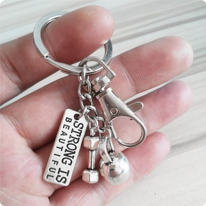 Detail of silver fitness keychain with dumbbell, kettlebell and Strong Is Beautiful tag