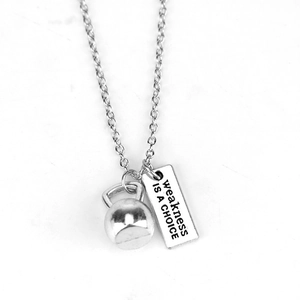 Macro detail of silver kettlebell pendant and engraved plaque saying Weakness is a Choice