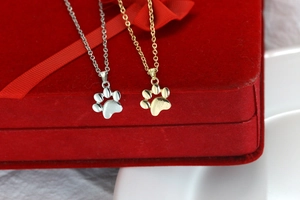 Close-up of gold and silver cat paw pendant necklaces on a red velvet jewelry box