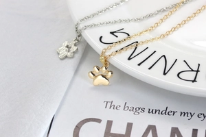 Detail view of gold and silver plated cute cat paw pendant necklaces on a white plate