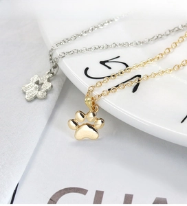 Close-up of cute cat paw pendant necklaces in gold and silver on a white ceramic plate
