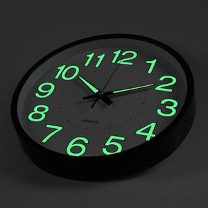 Primer plano de los números y manecillas luminosas de un reloj de pared negro