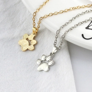 Detailed view of gold and silver paw print necklaces on a white plate and grey fabric