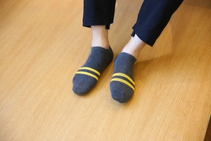 Dettaglio di calzini bassi in cotone grigio scuro con due strisce gialle sul legno
