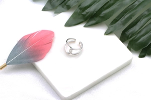Detail shot of a minimalist double-line cross silver ring on a white display stand