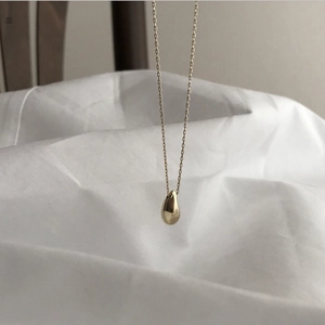 Detailed view of a gold teardrop pendant necklace hanging on a white cotton fabric background