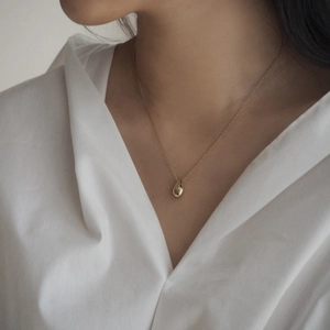 Detail of a minimalist gold teardrop pendant necklace on a model wearing white shirt