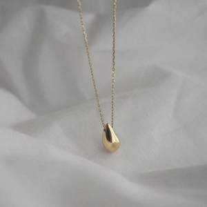 Macro shot of a minimalist gold teardrop pendant necklace on white fabric texture