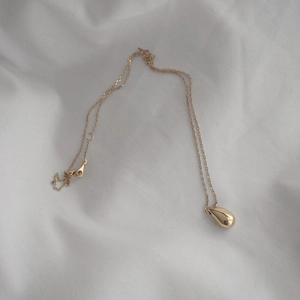 Detailed view of a gold teardrop pendant necklace on white textured fabric background