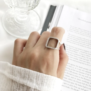 Lifestyle shot of a square pavé silver ring worn on index finger with aesthetic background