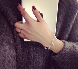 Detail of layered white pearl bracelet with gold chain and delicate V-shaped rings