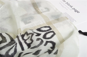 Detail of white cotton shawl with black abstract prints, gold stripes and black tassels