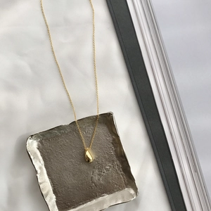 Detailed view of a gold teardrop pendant on a silver tray with minimalist silk backdrop