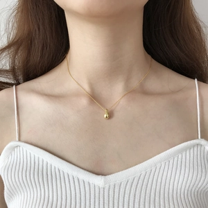 Close-up of minimalist gold teardrop pendant necklace worn on a white V-neck top