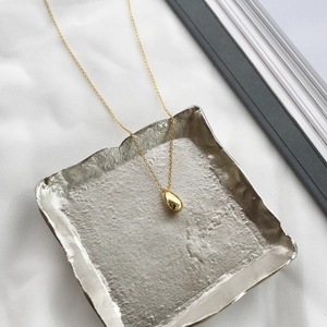 Macro shot of gold teardrop pendant on a hammered silver tray with white silk fabric
