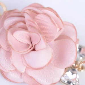 Portachiavi fiore in tessuto rosa con dettagli dorati e cristallo a cuore su sfondo grigio