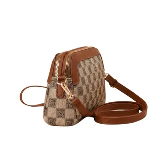Detail of checkered shoulder bag featuring dual zippers and adjustable brown leather strap