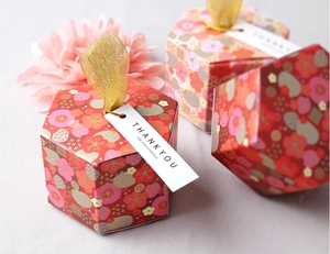 Hexagonal gift boxes with gold ribbon handles and floral patterns on soft fabric background