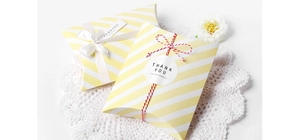 Macro detail of yellow striped pillow gift boxes with white silk bow and thank you tags