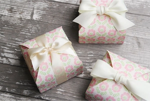 Detail of three floral paper gift boxes with beige ribbon bows on a rustic wood surface