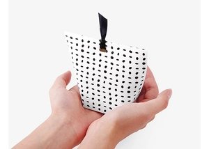 Close-up of hands holding a white pillow gift box with black polka dots and ribbon