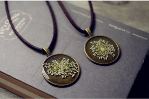 Vintage bronze circular pendant necklace with real dried lace flowers on old book background