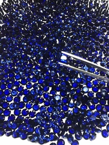Macro view of blue round faceted zircon stones being picked with silver metal tweezers