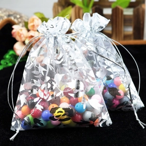 Close-up of white organza drawstring bags with silver floral prints and colored beads