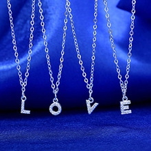 Detailed macro view of silver LOVE letter pendants with zircon inlay on blue silk fabric