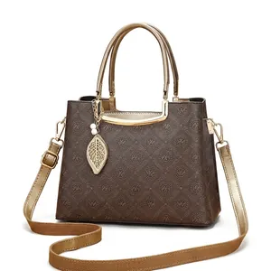 Detalle de bolso retro marrón con diseño floral, asa dorada y colgante en forma de hoja