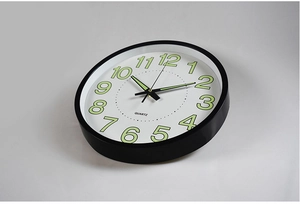 Side view of minimalist black wall clock with luminous green numbers and quartz movement