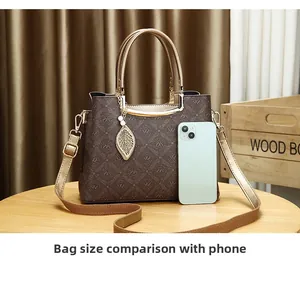 Comparación de tamaño del bolso monograma marrón junto a un smartphone en mesa de madera