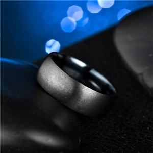 Close-up of matte black titanium steel ring with brushed finish on textured dark stones